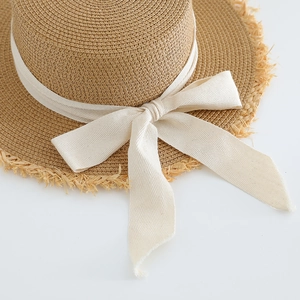 Detailed macro view of the natural straw weave and cream bow on the flat-top summer hat