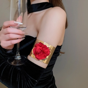 Detail of a golden metal arm cuff bracelet featuring a large red fabric rose floral design