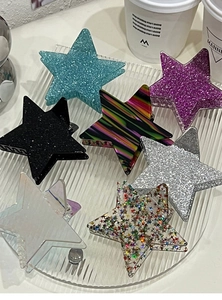 Flat lay of seven glitter and colorful star hair clips displayed on a rippled glass tray