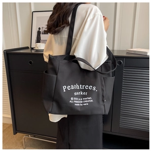 Close-up of black canvas tote bag with white lettering on a lifestyle model