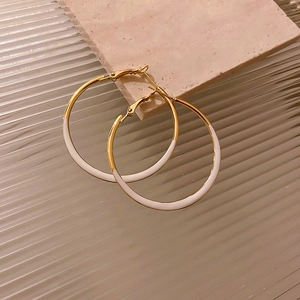 Detail view of large gold-plated hoop earrings with white enamel finish on stone background