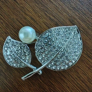 Spilla a foglia argentata con pavé di cristalli e perla bianca su fondo legno