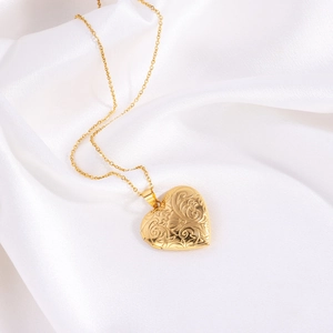 Détail macro du collier médaillon cœur doré avec relief floral sur soie blanche élégante