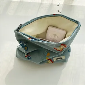 Detailed close-up of blue canvas makeup bag with exquisite butterfly embroidery and side label
