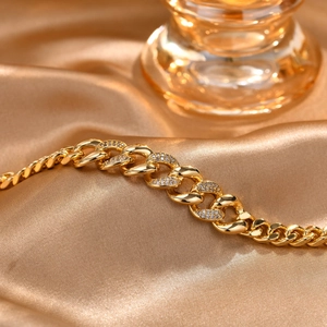 Nahaufnahme eines 18K Gold-Armbands mit Zirkonia-Besatz auf goldenem Seidenstoff