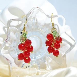 Elegant red berry drop earrings with green leaves and gold hooks on silk fabric