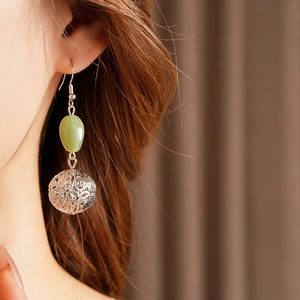 Close-up of green resin bead and silver hollow sphere earring worn by a model