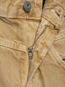 Detailaufnahme von Metallreißverschluss und Silberknopf an khakifarbener Jeanshose