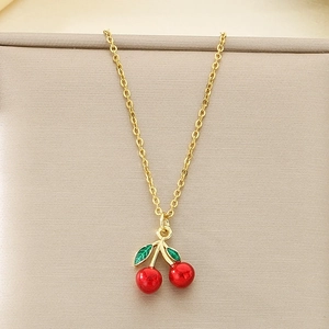 Close-up of golden necklace featuring a red enamel cherry pendant with green leaves