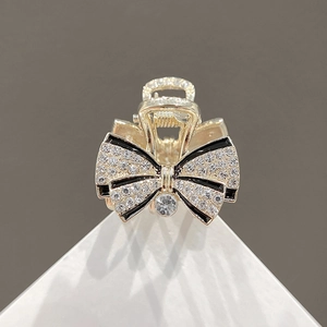 Exquisite golden bow hair claw clip with rhinestones and black borders on white stand