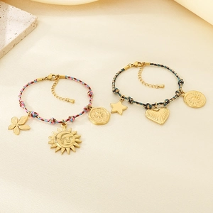 Detail of bohemian woven bracelets with golden sun and heart charms on a textured background