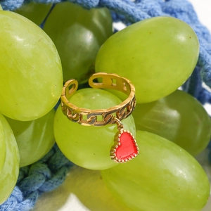 Primer plano de un anillo de cadena dorado con colgante de corazón rojo sobre uvas