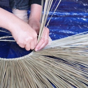 Detail van handen die een wandwaaier van natuurlijk zeegras handmatig vlechten en weven