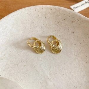 Detailed view of golden oval earrings with brushed texture on white ceramic tray