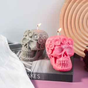 Detail view of lit skull candles with floral carvings in pink and grey colors