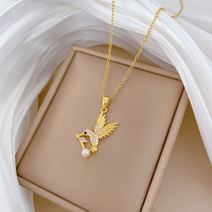 Détail du collier colibri doré avec zircons et perle blanche sur fond en soie élégant