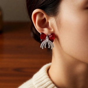Close-up of elegant red bow earrings with sparkling cubic zirconia tassels on a model