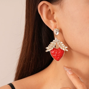 Detailed view of heart-shaped drop earrings with red resin and crystal wings