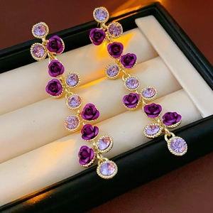 Gros plan de boucles d'oreilles rose dorée avec fleurs en émail violet et pompons en cristal