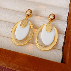 Close-up of gold-plated oval resin earrings with Hand Made tag on beige jewelry cushion