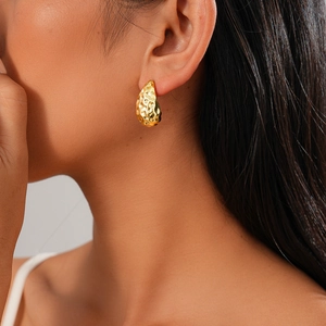 Gros plan sur des boucles d'oreilles goutte dorées avec texture en métal martelé
