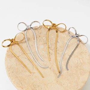 Elegant gold and silver bow drop earrings with snake chain texture on marble stand