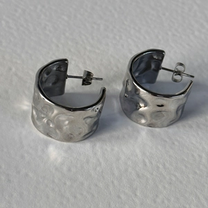 Close-up of silver C-shape earrings with hammered texture and polished metal surface