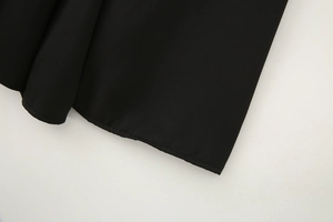 Close-up of the rolled hem stitching and plain weave fabric texture on a black midi dress