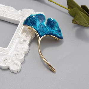 Elegant ginkgo leaf brooch in deep blue enamel with golden metal stem on white frame