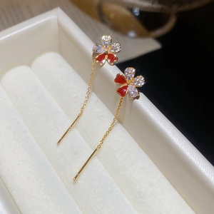 Close-up of gold-plated flower earrings with red enamel and zircon on white leather