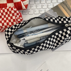 Detail of checkered velvet stationery pouch filled with pens in a cozy study setting