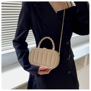 Detail of beige quilted box bag with woven handle and metallic chain strap on black suit