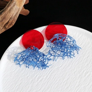 Détail de boucles d'oreilles en acrylique rouge et bleu avec dentelle vintage sur un plateau