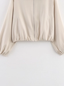 Detail view of the metal zipper and elastic hem on a beige flared baseball jacket
