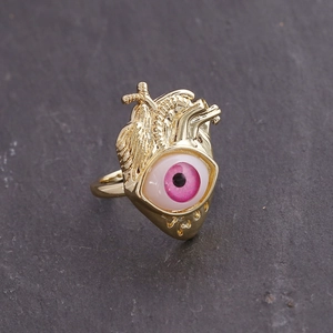 Close-up of 18K gold anatomical heart ring with pink eye detail on stone background