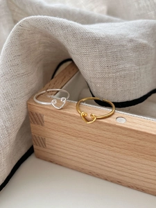 Detailed close-up of hollow heart rings in silver and gold on a wooden display stand