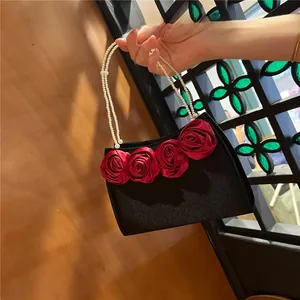 Detail of elegant black satin evening bag with red 3D fabric roses and pearl handle