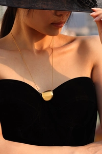 Polished 18K gold-plated circular pendant necklace worn by a model in black attire