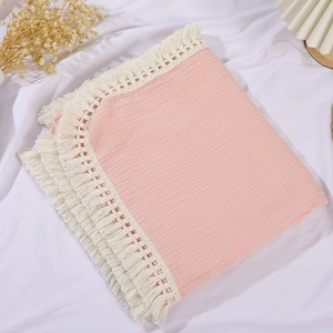 Detailed macro shot of pink double-layer muslin baby blanket with white tassel trim