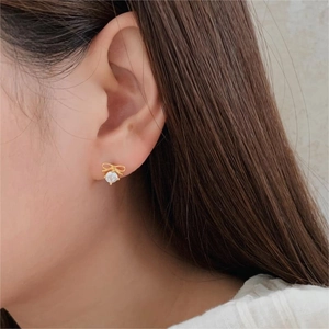 Elegant gold bow earrings with a central clear zircon on a model for a minimalist look