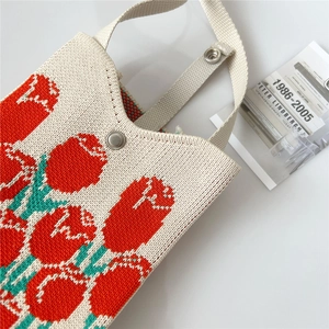 Close-up of cream knitted phone bag with red tulip floral pattern and snap button closure