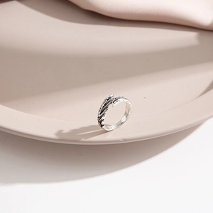 Detail view of silver feather wing ring on minimalist beige ceramic tray with soft fabric