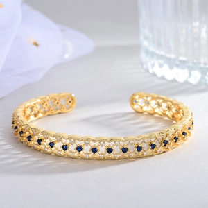 Detail of 18k gold plated open bangle with hollow mesh pattern and blue zircon inlay