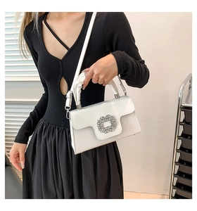 Detail of white glossy shoulder bag featuring crystal buckle and ruched handle