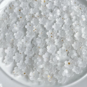 Detailed close-up of white translucent flower beads with golden glitter in a white bowl