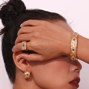 Detailed view of gold jewelry set with vintage texture, green gems and zircons on model