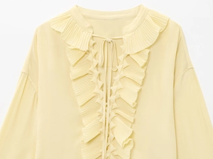 Detailed view of pale yellow top with layered ruffle neckline and tie-front closure