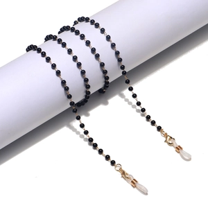 Handmade eyewear chain with black beads and gold links on white minimalist display stand