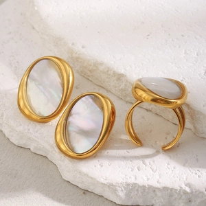 Detailed view of 18K gold-plated oval white shell earrings and open ring on a stone