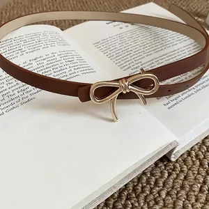 Vintage brown leather skinny belt with a gold bow buckle on a classic book background